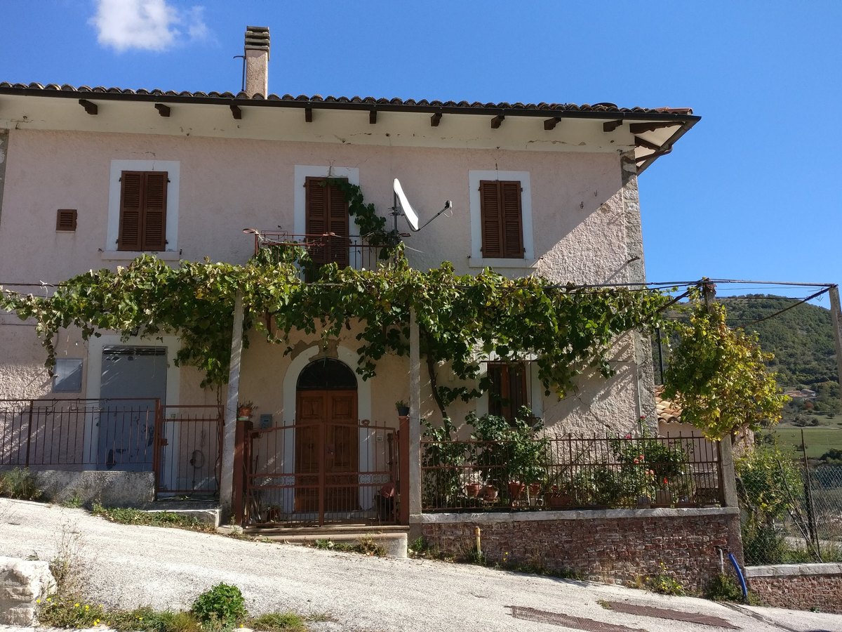Fabbricato residenziale a Croce di Visso prima dell&rsquo;intervento, con pergolato e ringhiera sul fronte principale